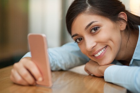 Closeup of smiling at camera attractive middle-aged Indian woman lying on counter and using...