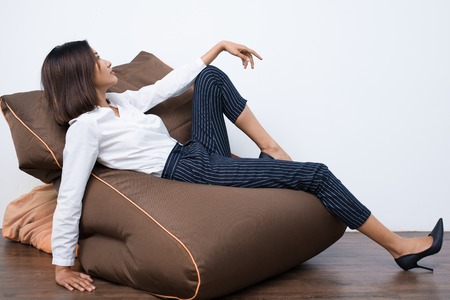 Pretty young Asian woman lying on beanbag chair in relaxed pose. Side view.の写真素材