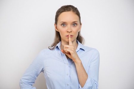Portrait of serious young woman looking straight and making silence gesture. Isolated view on white...