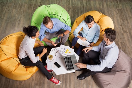Four active young people sitting on beanbag chairs around small table in cafe, working and discussing ideas. High angle view.の写真素材