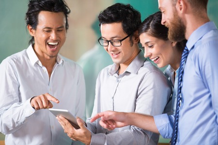 Cheerful business team pointing at tablet screen and laughing. Multiethnic group of people surfing the net. Teamwork or cooperation conceptの写真素材