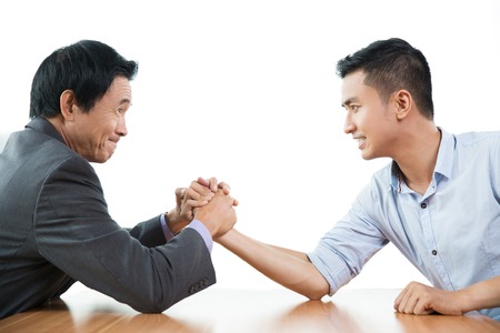 Senior and young business men arm wrestling aggressively at table and looking at each other. Isolated view on white background.の写真素材