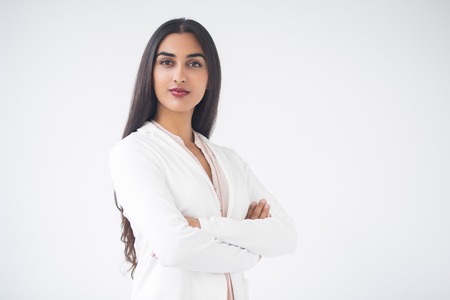 Closeup portrait of serious proud young gorgeous Indian business woman looking at camera and standing with arms crossed. Isolated view on white background.の写真素材