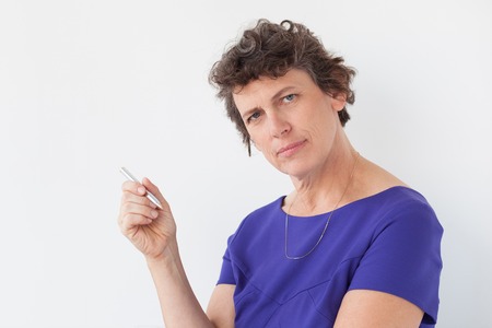 Closeup portrait of serious senior woman looking at camera and holding pen. Isolated view on white...