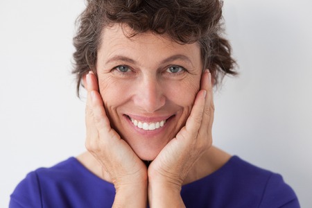 Closeup portrait of smiling senior woman looking at camera and touching her face. Isolated view on white background.の写真素材