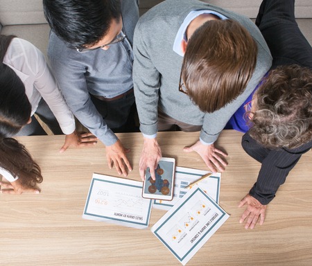 Closeup of business colleagues studying diagrams on tablet and papers. They are standing at table. Overhead view.の写真素材