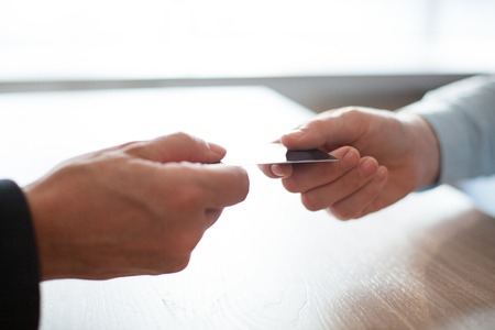 Close-up of male hand giving or passing credit card to another man above table. Unrecognizable businessman paying bill or getting new plastic card in bank. Banking conceptの写真素材