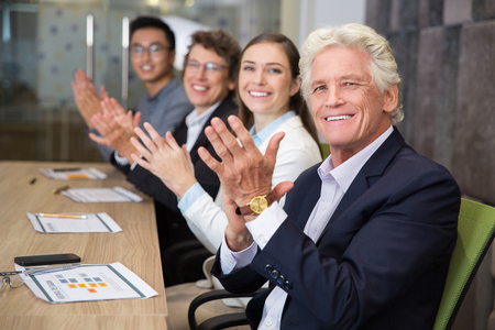 Group of four cheerful business people applauding and looking at camera. Portrait of satisfied colleagues sitting in row. Presentation or conference conceptの写真素材