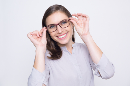 Studio portrait of happy young Caucasian woman wearing white shirt trying on eyeglasses, looking at camera and smilingの写真素材