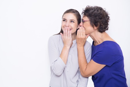 Studio portrait of senior woman wearing glasses whispering secret to her young daughter. Woman...