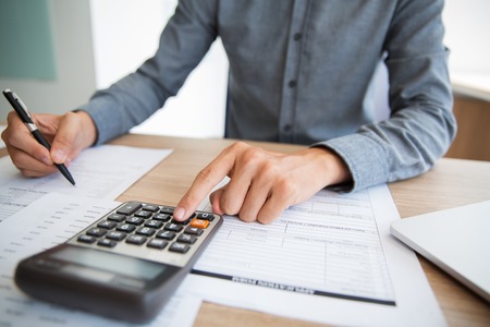Unrecognizable accountant examining financial report. Male hands using calculator at desk. Businessman preparing annual report in office. Paperwork conceptの写真素材