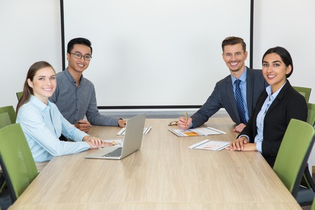 Group of four business people smiling at camera in board room. Confident team meeting to discuss business issues. Cheerful young managers sitting at table. Business conceptの写真素材