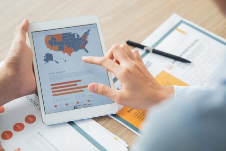 Hand of unrecognizable businessman holding digital tablet with USA map and chart. Hand of his female...