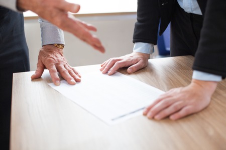 Unrecognizable business people discussing document. One person gesturing, other leaning on table....