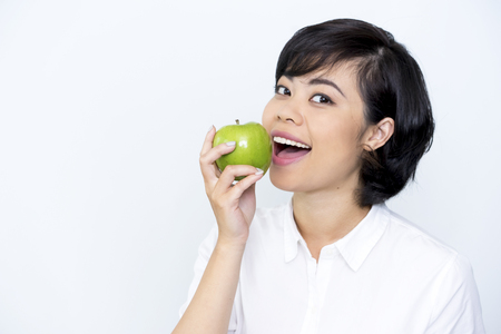 Portrait of positive Asian woman biting appleの写真素材