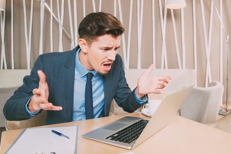 Indignant Businessman Working on Laptop in Cafeの写真素材