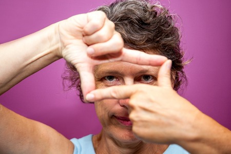 Portrait of creative woman looking through fingersの写真素材
