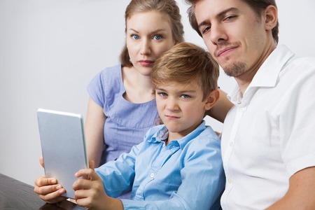 Mischievous little boy with touchpad and parentsの写真素材