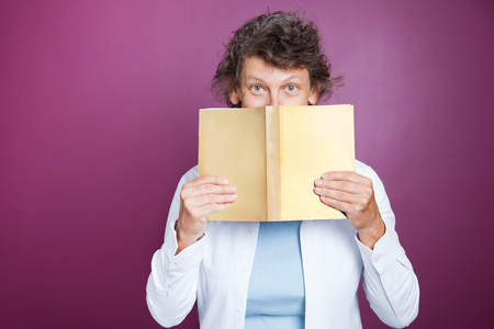 Closeup of Elderly Woman Hiding Behind Open Bookの写真素材