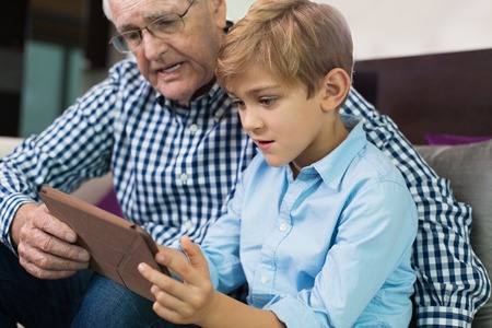 Positive little son and grandpa looking at photoの写真素材
