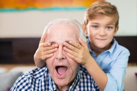 Smiling little boy covering eyes of grandfather