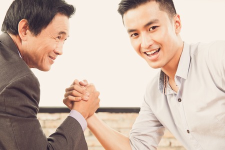 Happy young and senior businessmen arm-wrestlingの写真素材