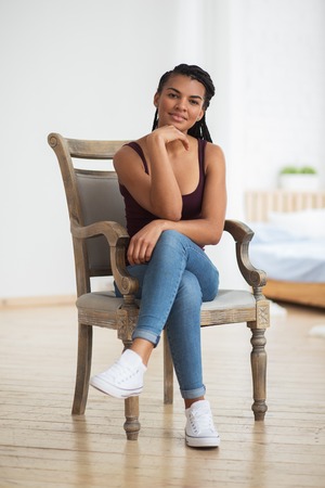 Pensive young woman looking at camera in armchairの写真素材