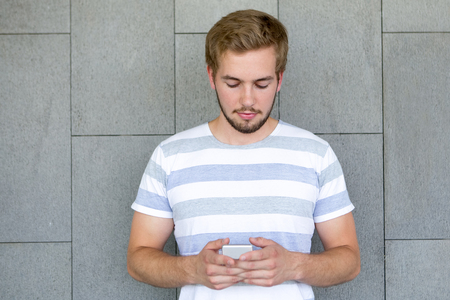 Serious young man texting message standing at wallの写真素材