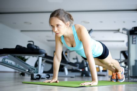 Serious young woman doing push-ups on mat in gymの写真素材