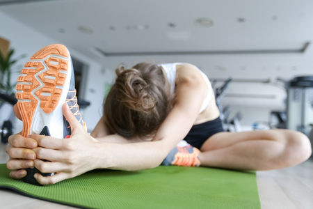 Sneaker of young woman stretching leg in gym