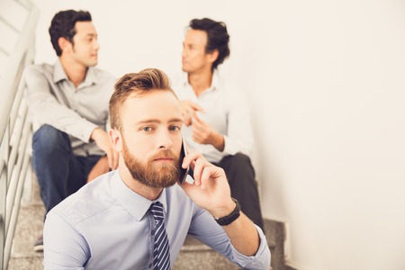 Serious bearded man using phone sitting on stairsの写真素材