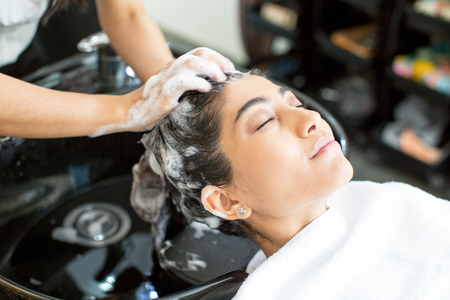 Hairdresser washing hair of enjoying young womanの写真素材