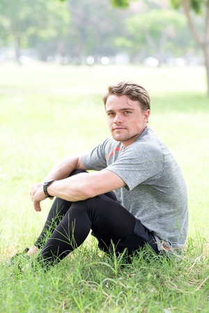 Content Young Sporty Man Sitting on Grass in Parkの写真素材