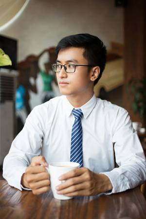 Pensive Asian businessman with mug looking asideの写真素材
