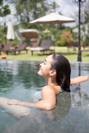 Happy young woman relaxing in hotel swimming poolの写真素材
