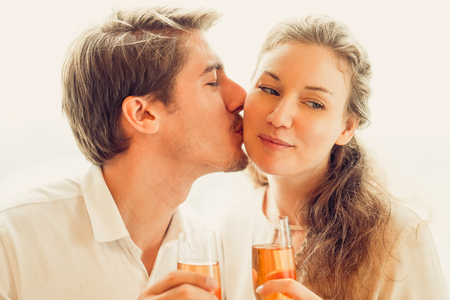 Portrait of happy young Caucasian man kissing his girlfriend at romantic date. Young couple holding champagne flutesの写真素材