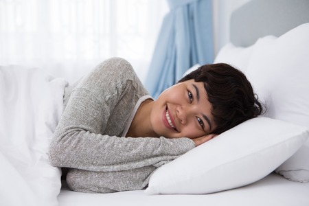Smiling Young Asian Woman Lying in Bedの写真素材