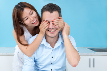 Smiling Woman Covering Husband Eyes in Kitchenの写真素材