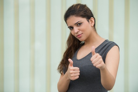 Confident young woman showing thumbs up outdoorsの写真素材