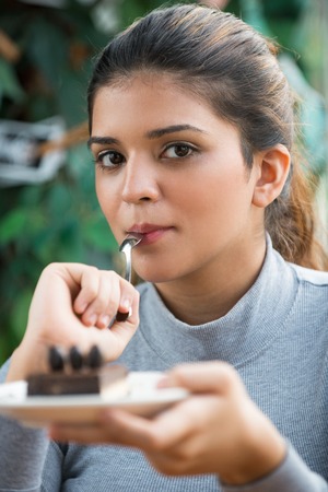 Flirty woman eating cake and looking at cameraの写真素材