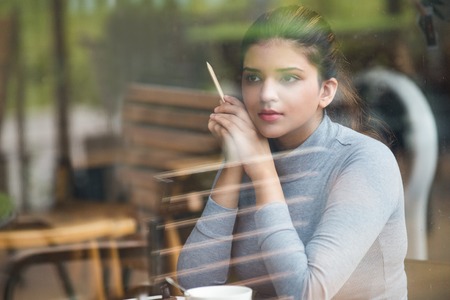 Dreamful young student with pencil sitting in cafeの写真素材