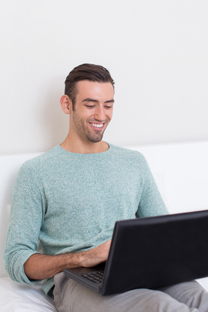 Happy Young Man Working on Laptop on Sofaの写真素材
