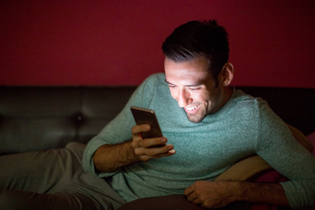 Laughing Man Using Smartphone on Sofa at Nightの写真素材