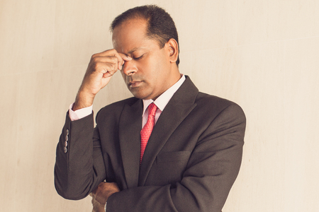 Tired businessman rubbing eyes standing at wallの写真素材