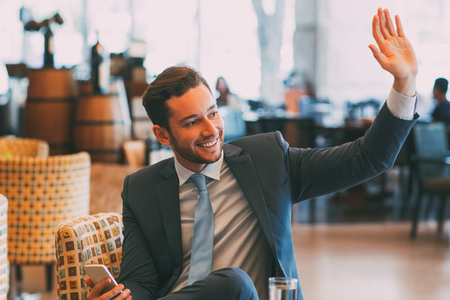 Joyful Business Man Waving to Someone in Cafeの写真素材