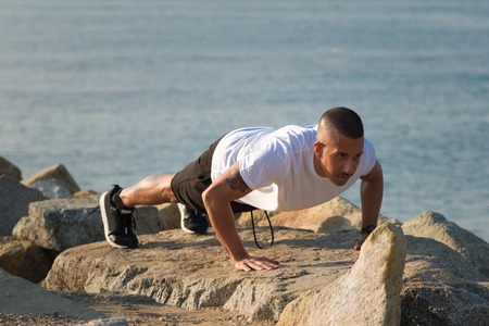 Strong young man performing push-ups on stone