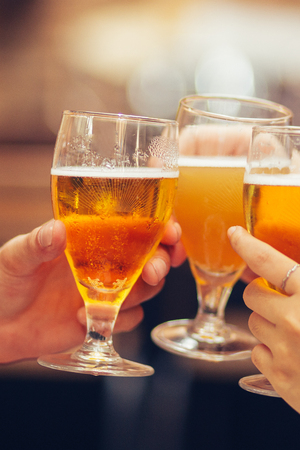 Closeup of three hands holding glasses of beer and clinking themの写真素材