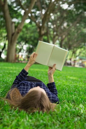 Young Girl Lying on Grass and Reading Bookの写真素材