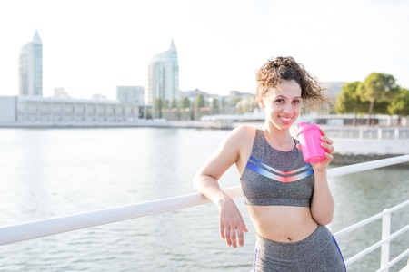 Smiling Pretty Sporty Girl Drinking by City Riverの写真素材