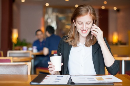 Happy Woman Working and Calling on Phone in Cafeの写真素材